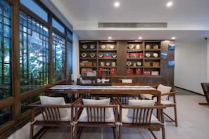 A dining area with a table and chairs, a bookshelf with various items, and large windows.