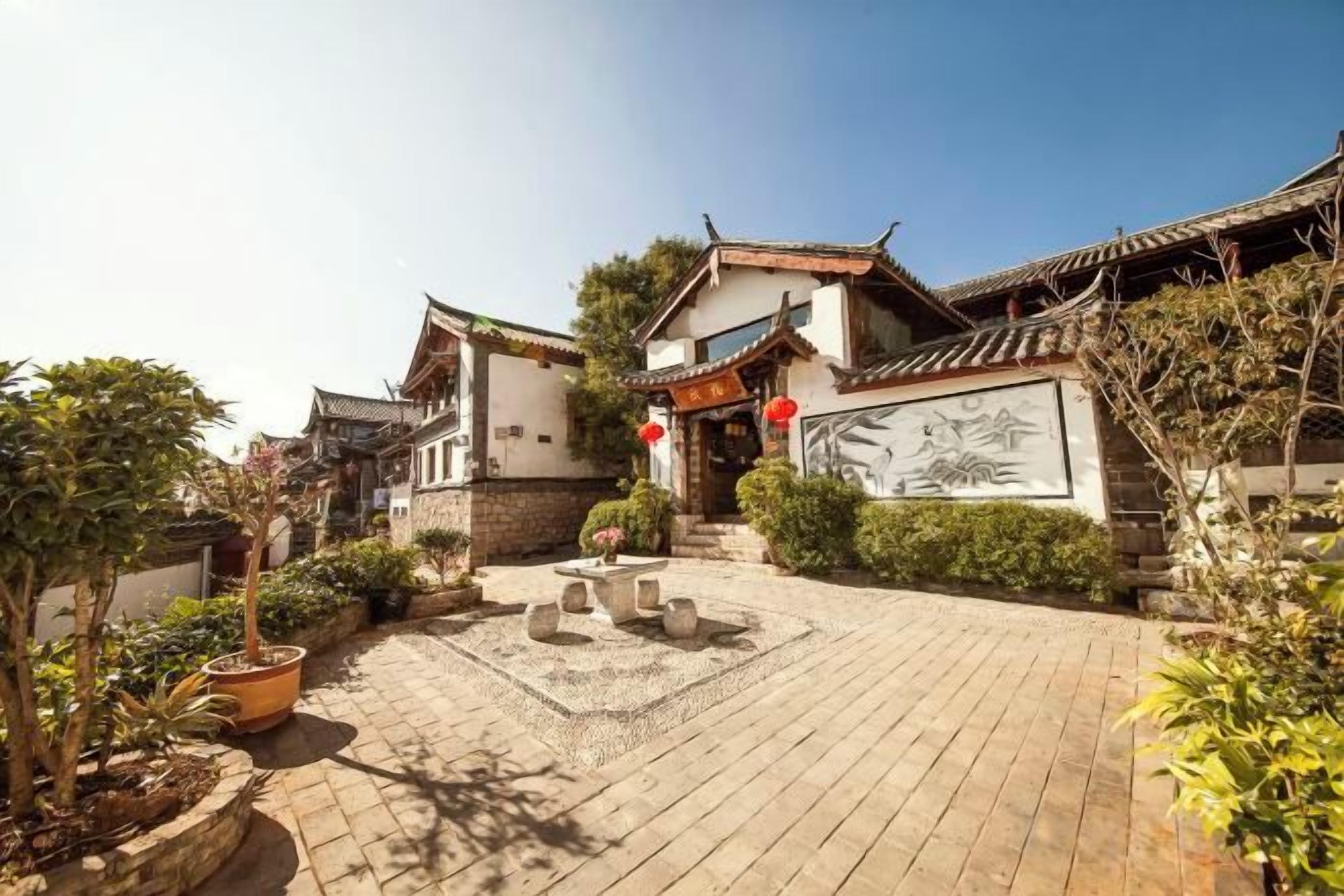A traditional courtyard with a tiled floor, stone benches, and potted plants.