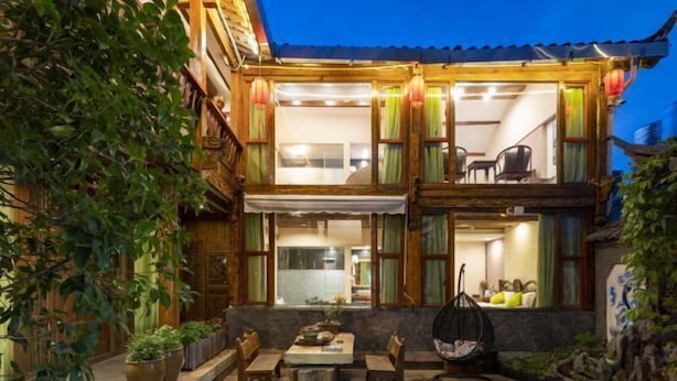 A traditional wooden house with a balcony, a dining area with a table and chairs, and potted plants.