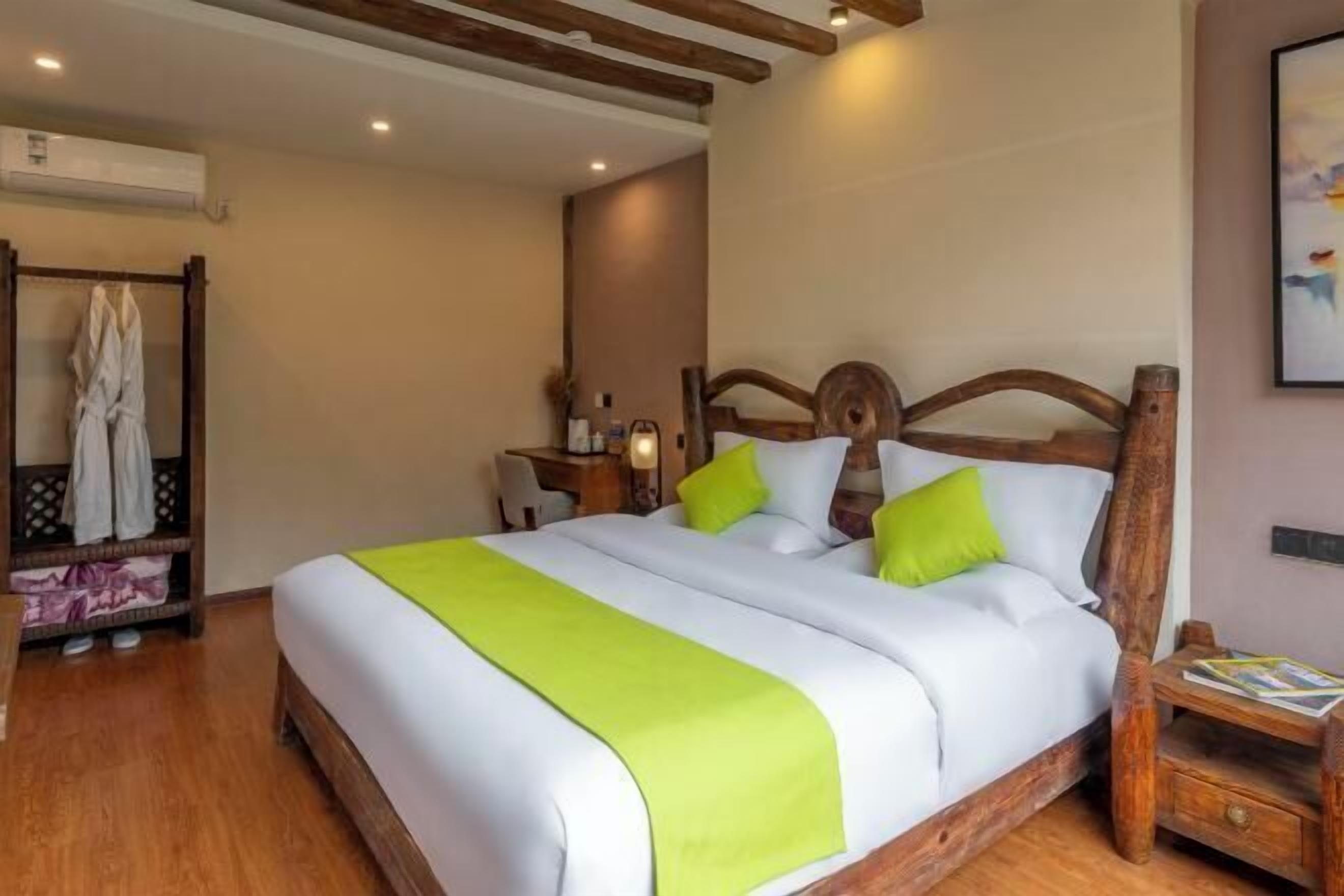 A hotel room with a wooden bed frame, white bedding, and a green throw.