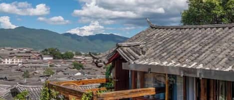 A traditional building with a tiled roof, wooden balcony, and a view of surrounding structures and mountains.