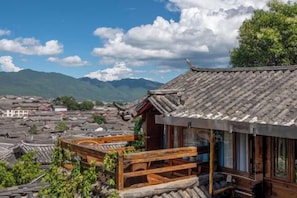 A traditional building with a tiled roof, wooden balcony, and a view of surrounding structures and mountains. - Lijiang Houfu Inn (Lijiang)