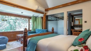A bedroom with a bed, a window with curtains, a wooden headboard, a small table, and a view of the outdoors.