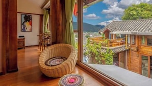 A room with a large window, a wicker chair, a woven mat, and traditional architecture visible through the window.