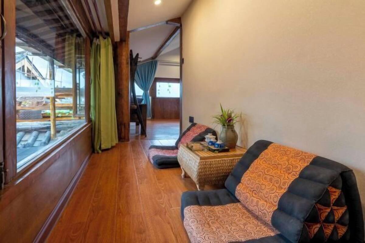 Ein Zimmer mit Holzboden, einer Couch, einem kleinen Beistelltisch und einem Fenster mit Vorhängen.
