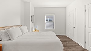 Un dormitorio con una cama, una mesita de noche, una lámpara, una ventana y una puerta.