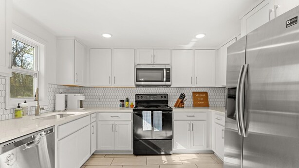 Una cocina moderna con gabinetes blancos, electrodomésticos de acero inoxidable y salpicadero de azulejos.