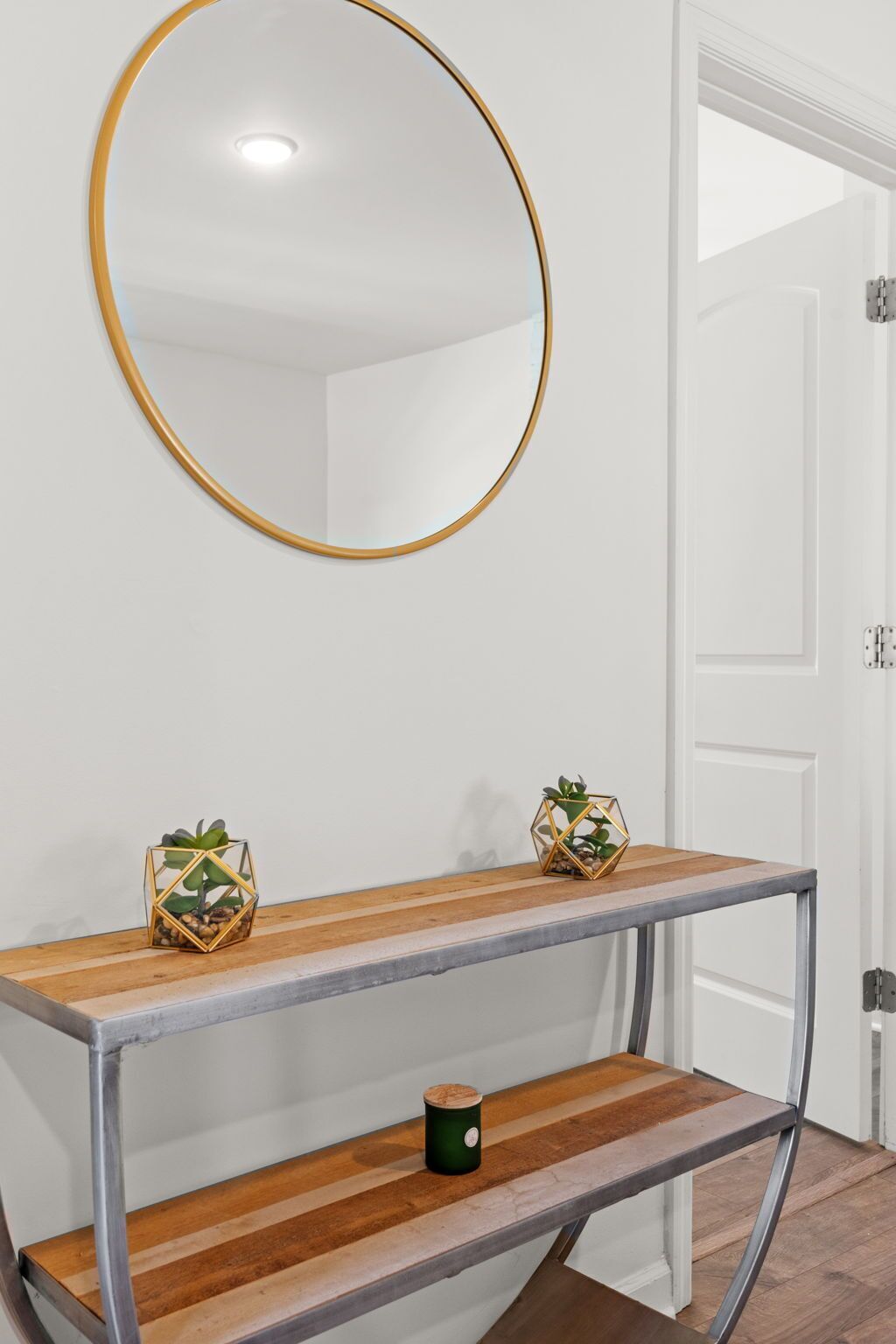 A room with a round mirror, a wooden console table with metal legs, and two decorative plants.