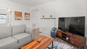 Una sala moderna con un sofá gris, una mesa de centro de madera, un televisor de pantalla plana y una chimenea.