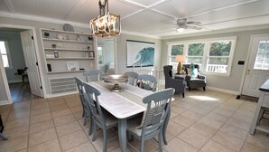 A dining area with a table and chairs, a ceiling fan, and a large window with a view of greenery. - Game Time - Channel Front in Garden City Beach (Garden City Beach)