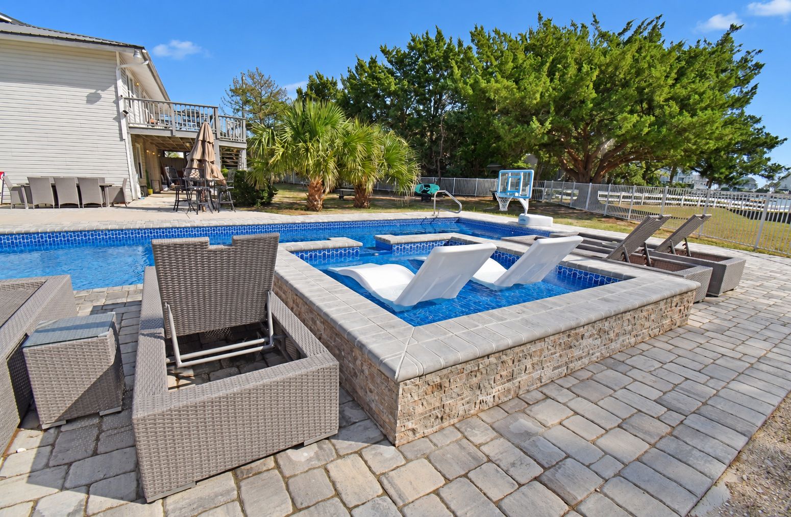 A swimming pool with lounge chairs and a hot tub area.