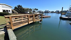 A wooden dock extending into calm water with boats docked nearby. - Game Time - Channel Front in Garden City Beach (Garden City Beach)