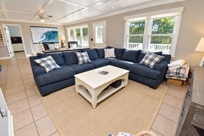 A living room with a sectional sofa, a coffee table, and a large window. - Game Time - Channel Front in Garden City Beach (Garden City Beach)