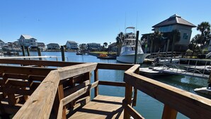A wooden pier leading to a marina with boats and houses in the background. - Game Time - Channel Front in Garden City Beach (Garden City Beach)