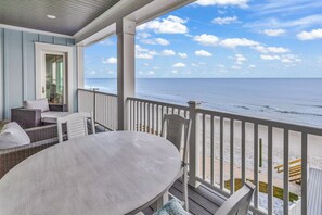 A covered outdoor area with a table and chairs, a view of the beach, and a wooden deck. - Jonesin' By The Beach - Ocean Front & Channel Front in Garden City Beach (Garden City Beach)