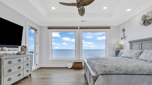 A bedroom with a large bed, a dresser, a television, and a view of the ocean through large windows. - Jonesin' By The Beach - Ocean Front & Channel Front in Garden City Beach (Garden City Beach)