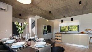 A modern kitchen with a central island, a dining area with a table set for four, and a view of the outdoors through large windows. - Amazing home in Visnjan (Visnjan)