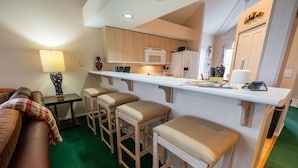 Ett kompakt bostadsutrymme med ett litet kök, en soffa, ett soffbord och en barstol.