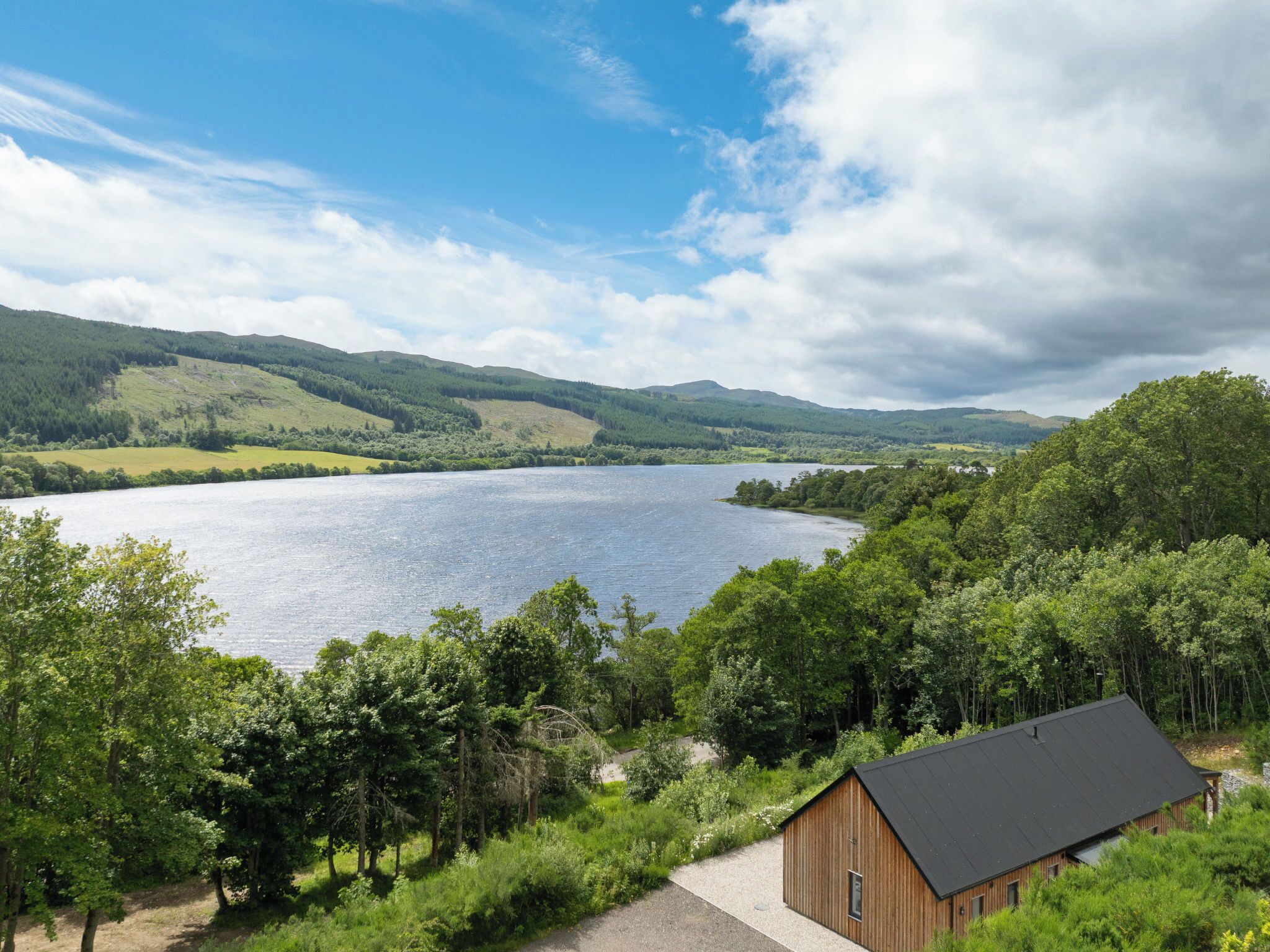 A lakeside cabin with a gravel path leading to it, surrounded by lush greenery and hills.