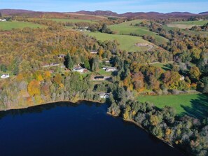 Vue aérienne d’une propriété au bord d’un lac, comprenant plusieurs maisons, entourée d’arbres aux couleurs automnales et de collines ondulantes.