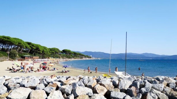 A beach with rocky foreground, clear blue sky, and calm sea. - La Casetta dei Pescatori by Interhome (Follonica)