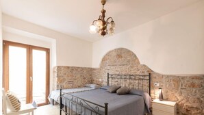 A bedroom with a stone wall, a bed with a metal frame, a nightstand with a lamp, and a wooden chair. - La Casetta dei Pescatori by Interhome (Follonica)