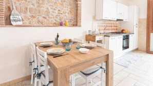 A cozy kitchen with a stone wall, white cabinets, and a wooden dining table. - La Casetta dei Pescatori by Interhome (Follonica)
