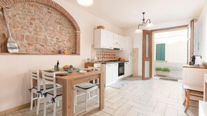 A modern kitchen with white cabinets, a wooden dining table, and a stone backsplash. - La Casetta dei Pescatori by Interhome (Follonica)