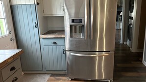 A modern kitchen with a stainless steel refrigerator, wooden cabinets, and a herringbone-patterned floor. - Out in Left Field Home in Country Farm setting  (Laurens)