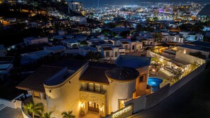Un hotel costero con piscina, un camino de entrada curvo y vistas de la ciudad de noche.