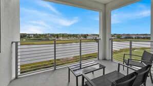 Un balcon donnant sur un parking et sur des bâtiments situés au loin.