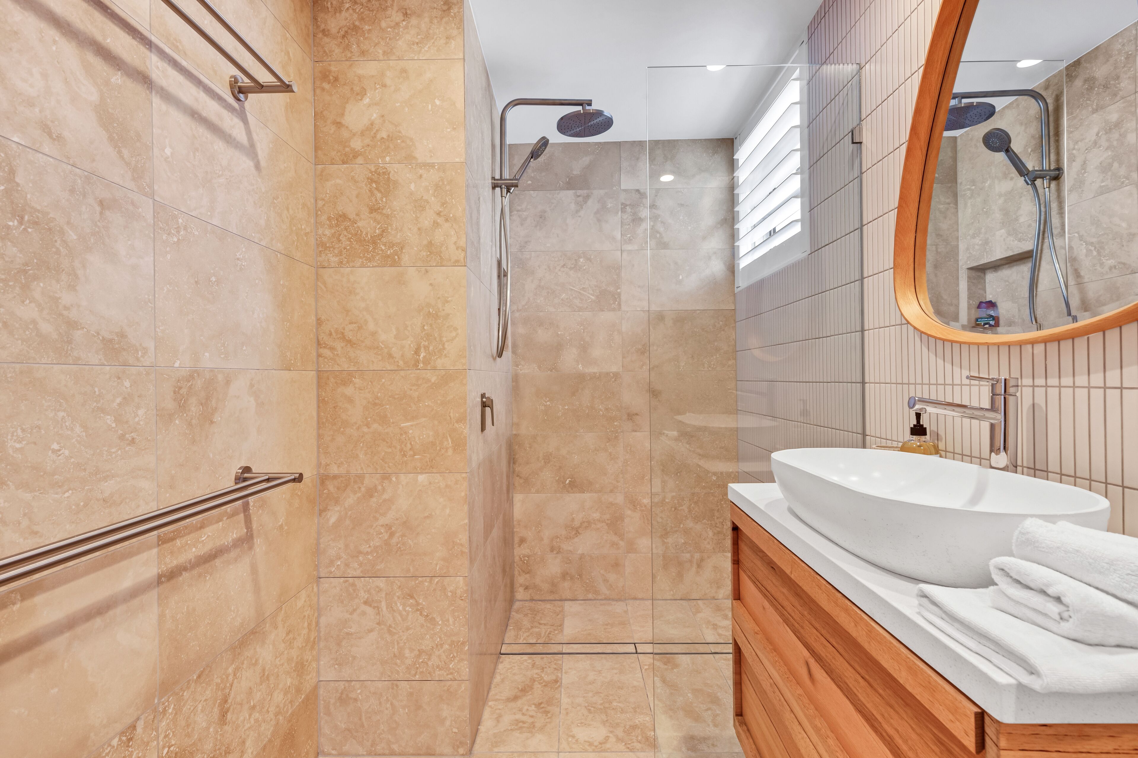 A modern bathroom with a large oval sink, a wooden vanity, a glass shower enclosure, and a mirror with a wooden frame.