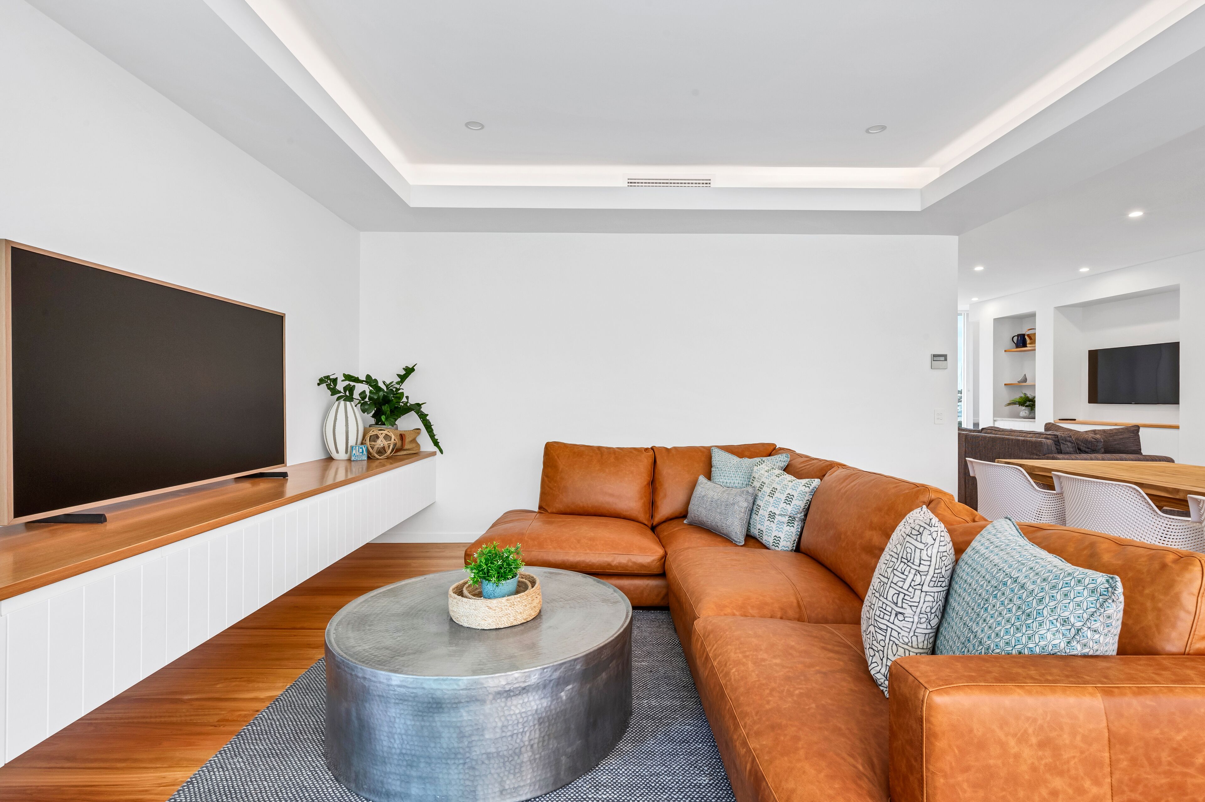 A modern living room with a large flat-screen TV, a leather sofa, a round coffee table, and a small plant.