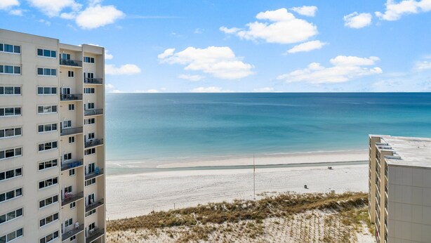 Un hotel frente a la playa con varios pisos, balcones y vista al océano.