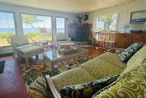 Een woonkamer met een bank, stoelen, een open haard en uitzicht op de oceaan.