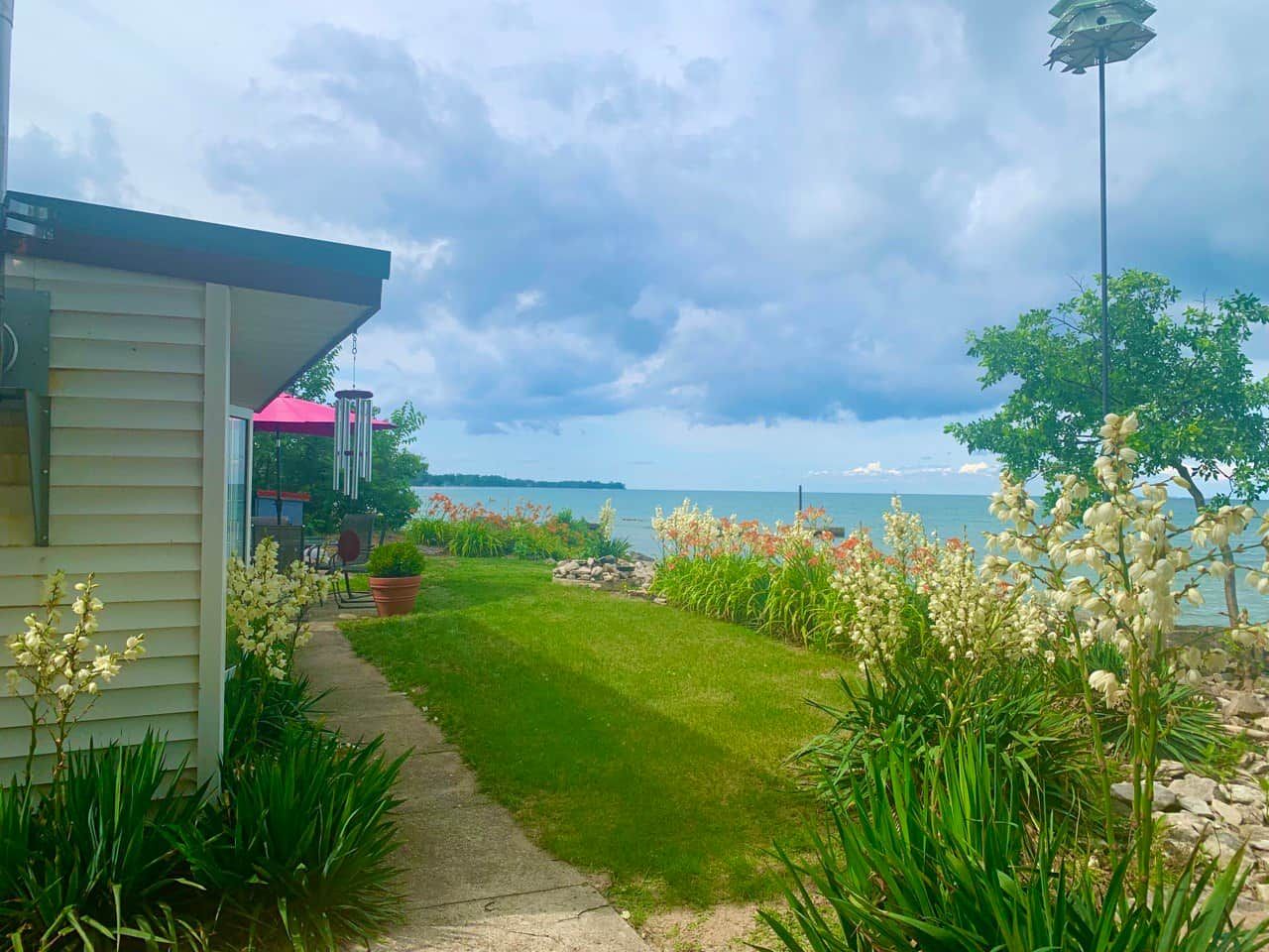 Une propriété située en bord de mer, avec un chemin pavé menant à une zone herbeuse, une petite maison dotée d’un porche et une vue sur la mer.