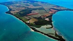 Ett flygbildsbild av ett kustområde med tydliga gränser mellan land och vatten, inklusive en strand och åkermark.