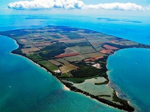 Luchtbeeld van een kustgebied met duidelijke land- en watergrenzen, inclusief een strand en landbouwvelden.
