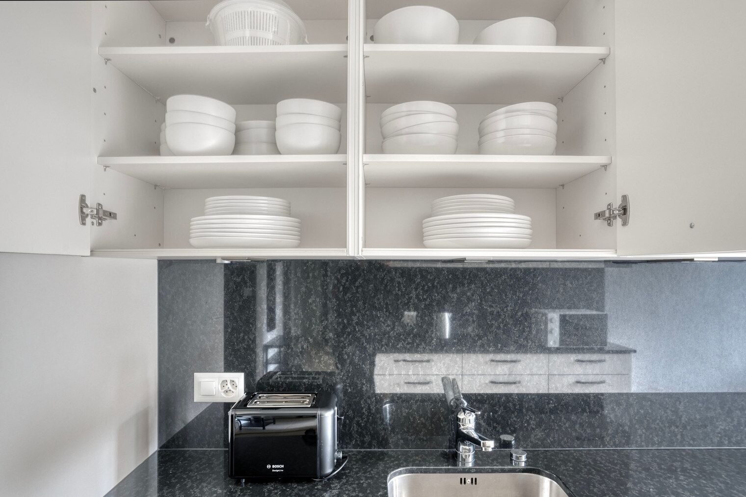 A kitchen with white cabinets, a Bosch toaster, a sink, and a granite countertop.