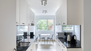 Una cocina moderna con armarios blancos, encimera negra, un lavabo, microondas, hervidor y una ventana que proporciona luz natural.