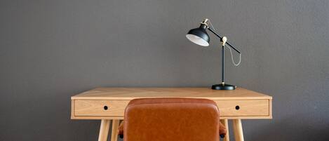 A wooden desk with a black desk lamp, a brown leather chair, and a grey wall.