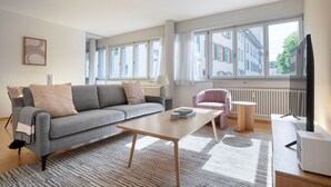 A modern living room with a grey sofa, a wooden coffee table, and a pink armchair.