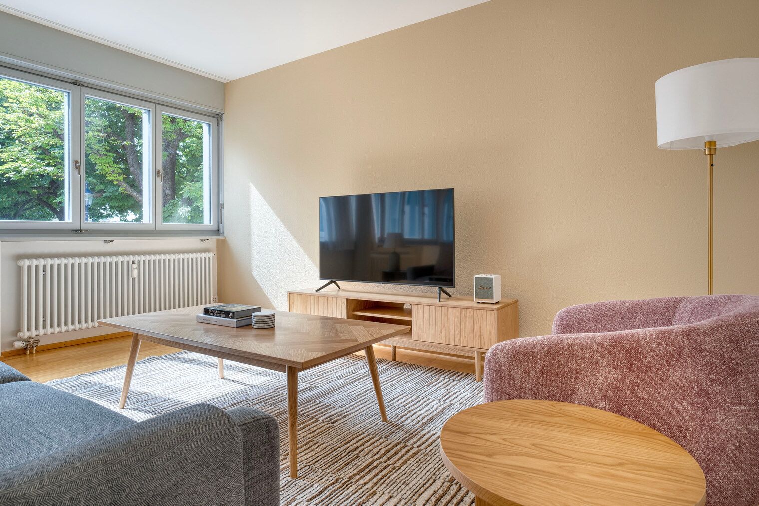 A modern living room with a TV, wooden furniture, and a large window.