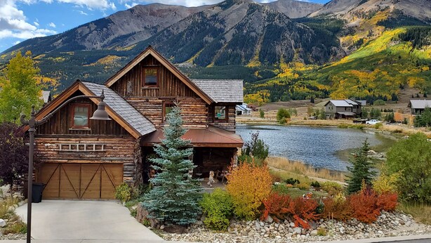Un rustico chalet in legno con un garage, un piccolo portico e vista su un lago e montagne.