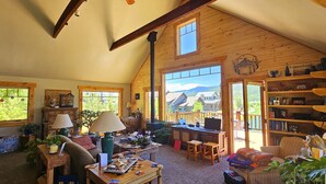 Un ambiente accogliente e rustico con travi in legno, un'ampia finestra che si affaccia su un paesaggio suggestivo, una scrivania di legno con un portatile e una libreria piena di libri.
