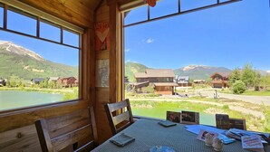 Una baita di legno con tavolo e sedie, un poster appeso al muro e vista su un lago e montagne.