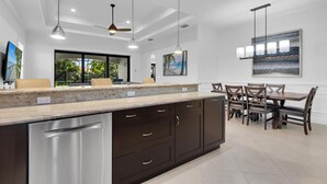 Eine moderne Küche mit Granit Arbeitsplatte, dunklen Schränken und Edelstahlgeräten. Es gibt eine Essecke mit Tisch und Stühlen, und ein großes Fenster mit Blick auf Grünflächen.