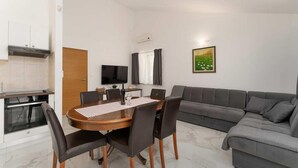 Ein modernes Wohnzimmer mit Essbereich, einem grauen Sofa, einem Flachbildfernseher und einem Gemälde an der Wand.