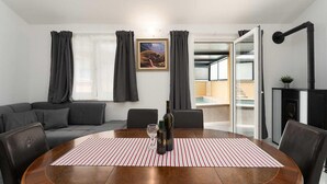 Ein modernes Wohnzimmer mit einem runden Holztisch, grauen Sofas und einem großen Fenster mit Vorhängen.