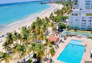 A beachside hotel with a swimming pool, palm trees, and a view of the ocean.